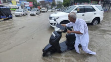 An elderly man pushes his scooter on a waterlogged road