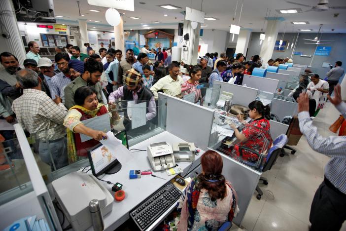 People stand in queues at cash counters to deposit and withdraw money inside a bank in Chandigarh